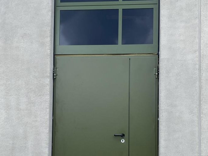 Grüne Stahltür mit Oberlicht an einer Betonfassade